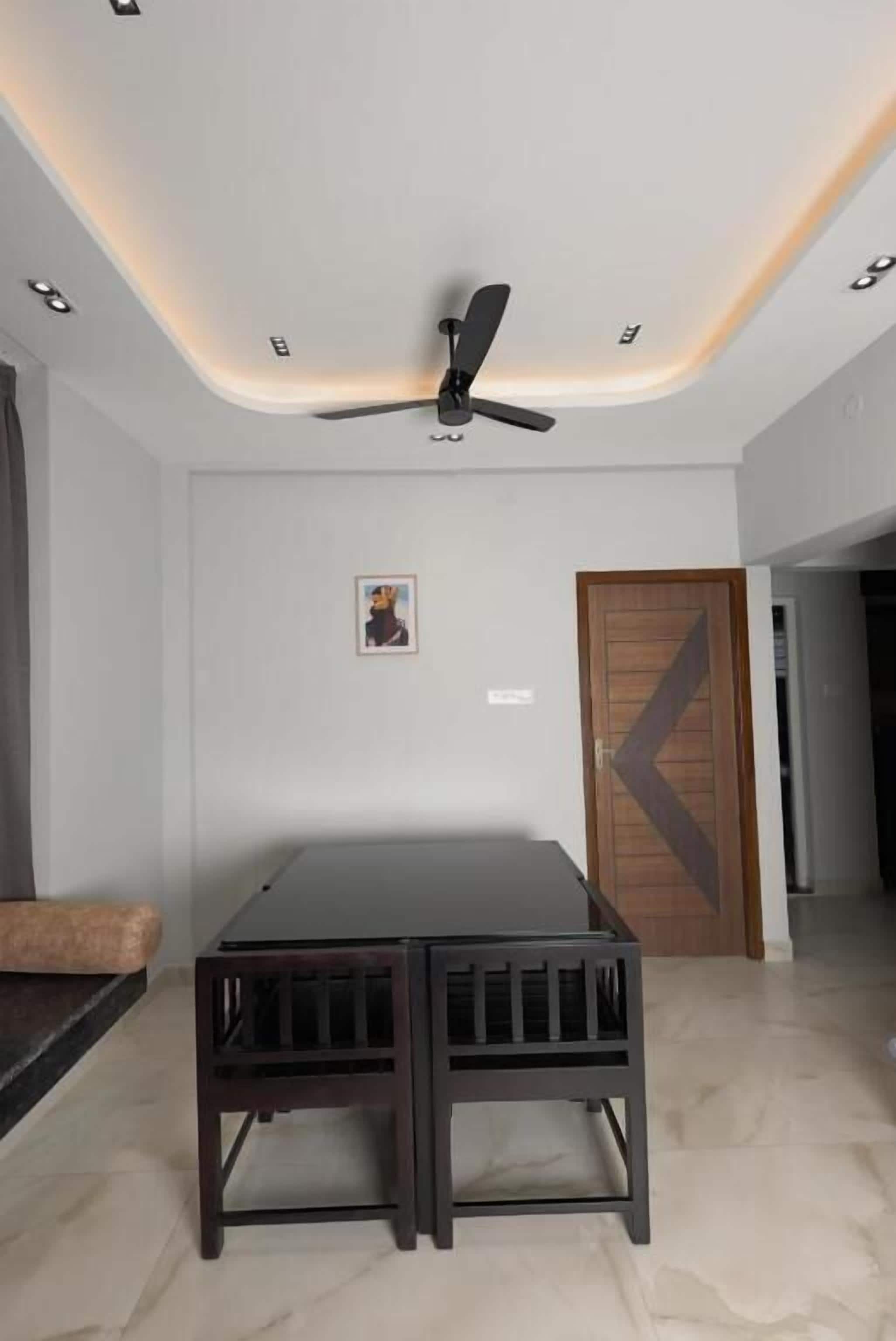 A room with a ceiling fan, a wooden door, a small table, and a framed picture on the wall.