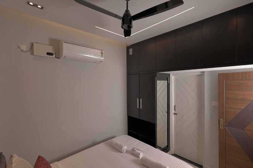 A bedroom with a bed, a ceiling fan, an air conditioning unit, and a wardrobe.