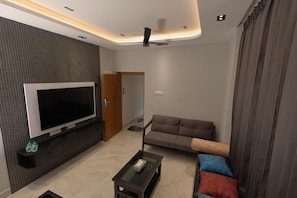 Uma sala de estar moderna com televisão de tela plana, um sofá, uma mesa de centro e um ventilador de teto.