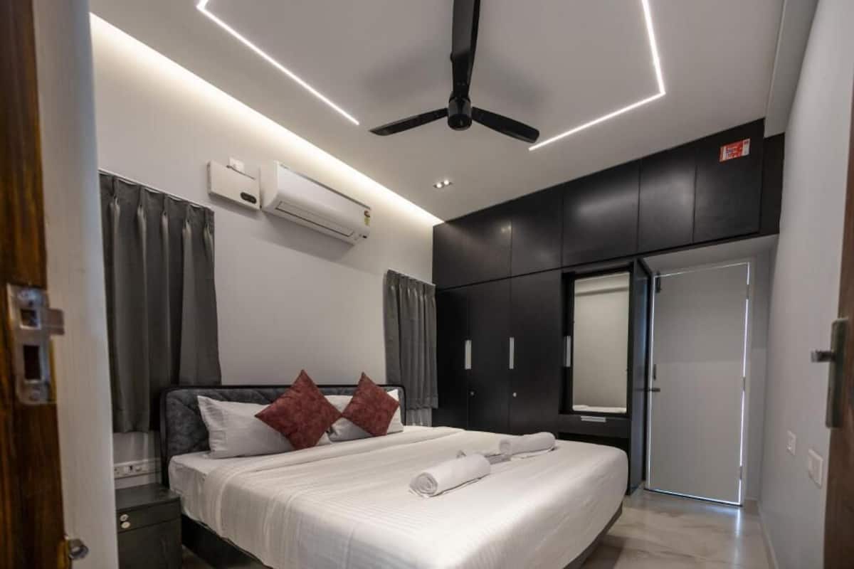 Quarto moderno com cama, ar condicionado, ventoinha no teto e guarda-roupa.
