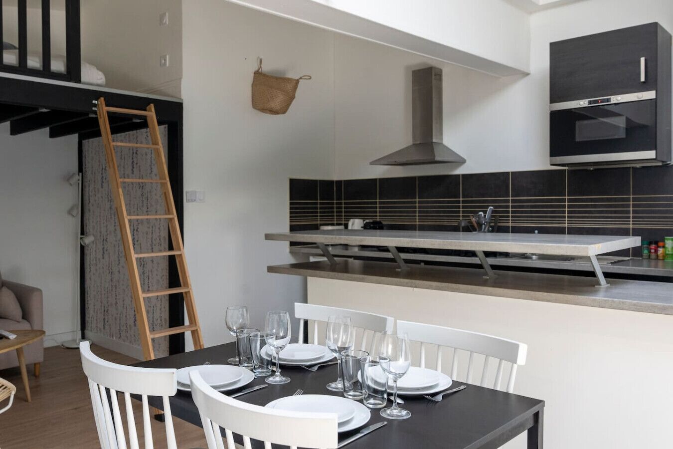 Una cocina moderna con horno empotrado, un colgador para ollas y un comedor con mesa dispuesta para cuatro.