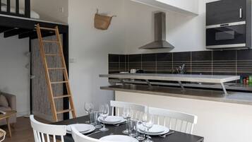 Una cocina moderna con horno empotrado, un colgador para ollas y un comedor con mesa dispuesta para cuatro.