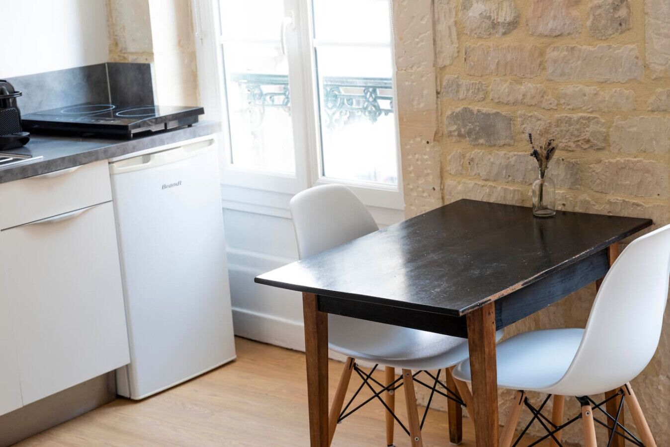 Une cuisine avec un plan de travail noir, des meubles blancs, un lave-vaisselle blanc et une table à manger avec deux chaises blanches.