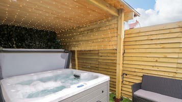 Un jacuzzi con escalones, un sofá de mimbre y una valla de madera con luces de cuerda.