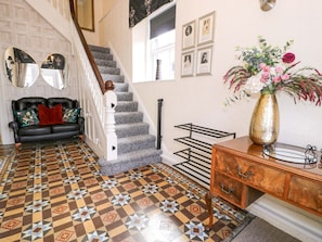 Una escalera con suelo estampado, un sofá de cuero negro, un aparador de madera y una pared con cuadros enmarcados.