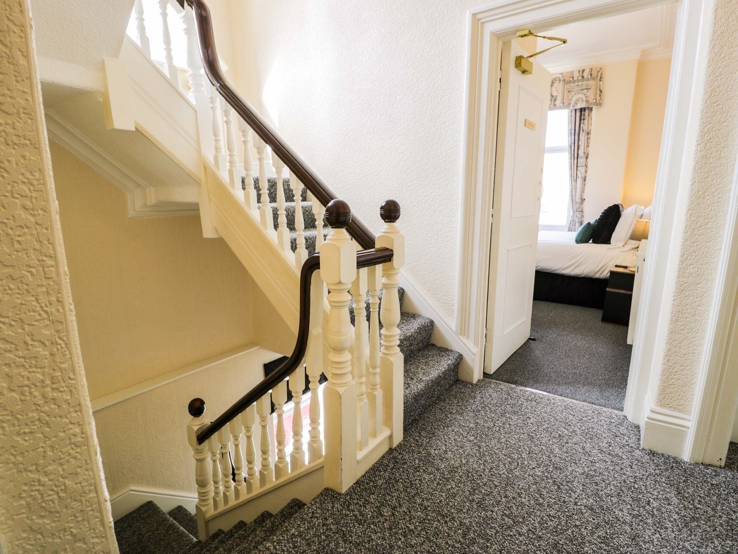 A staircase with white balusters and dark handrails leading to a bedroom with a bed and a nightstand.