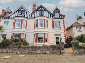 A multi-story building with a bay window, a stone wall in front, and a clear sky. - The Causeway (Llandudno)