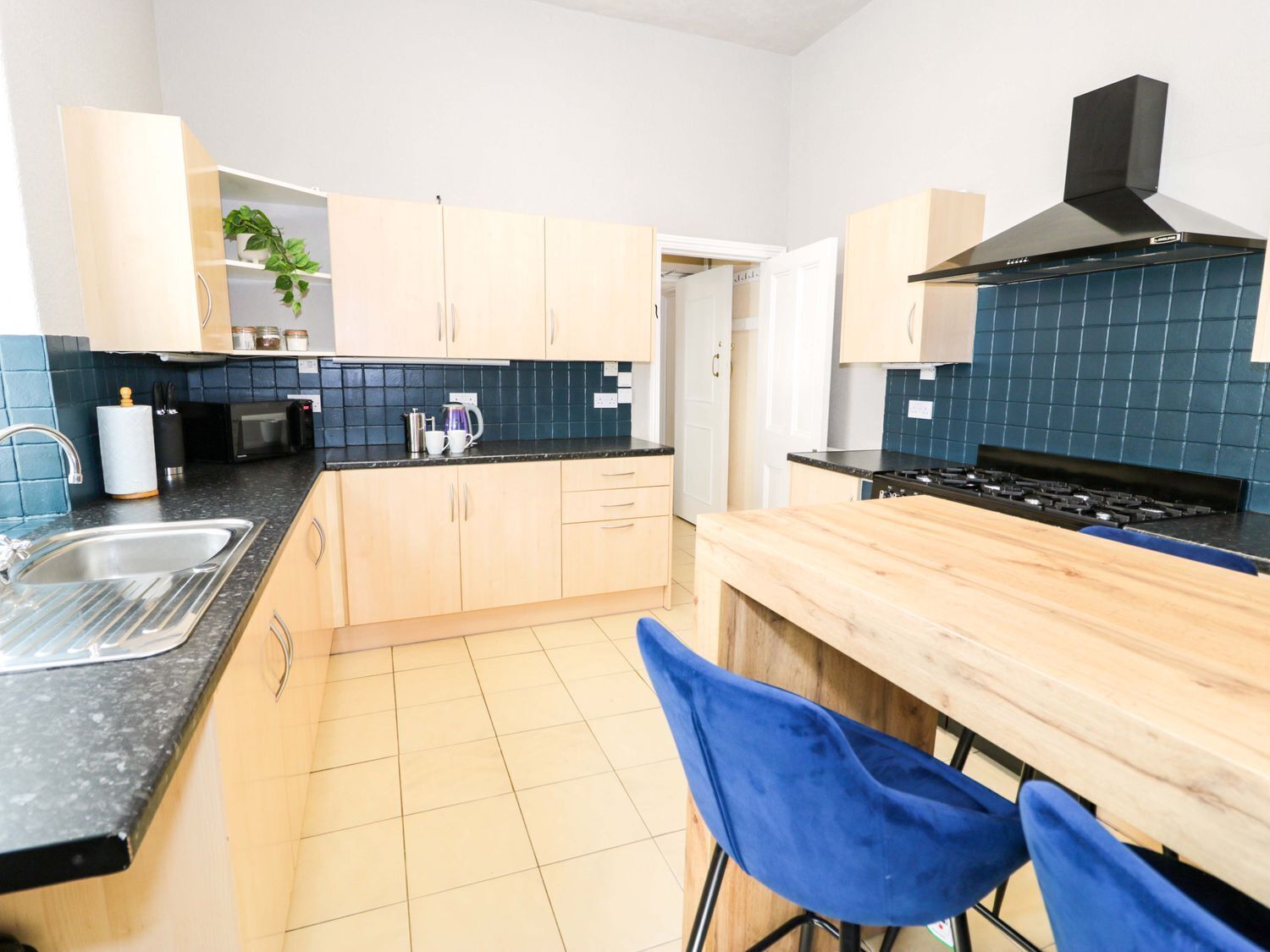 A modern kitchen with light wooden cabinets, a black stove, and a blue tiled backsplash.