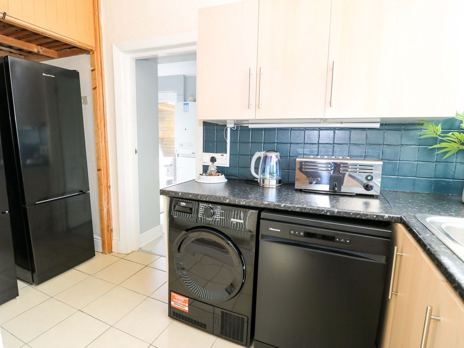 A compact kitchen with a black dishwasher, a compact washer, a toaster, and a kettle on the countertop.
