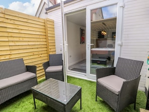 A patio with wicker furniture, a glass table, and a sliding glass door leading to a room. - The Causeway (Llandudno)
