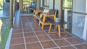 A covered patio with wooden chairs, a small table, and a view of the outdoors.