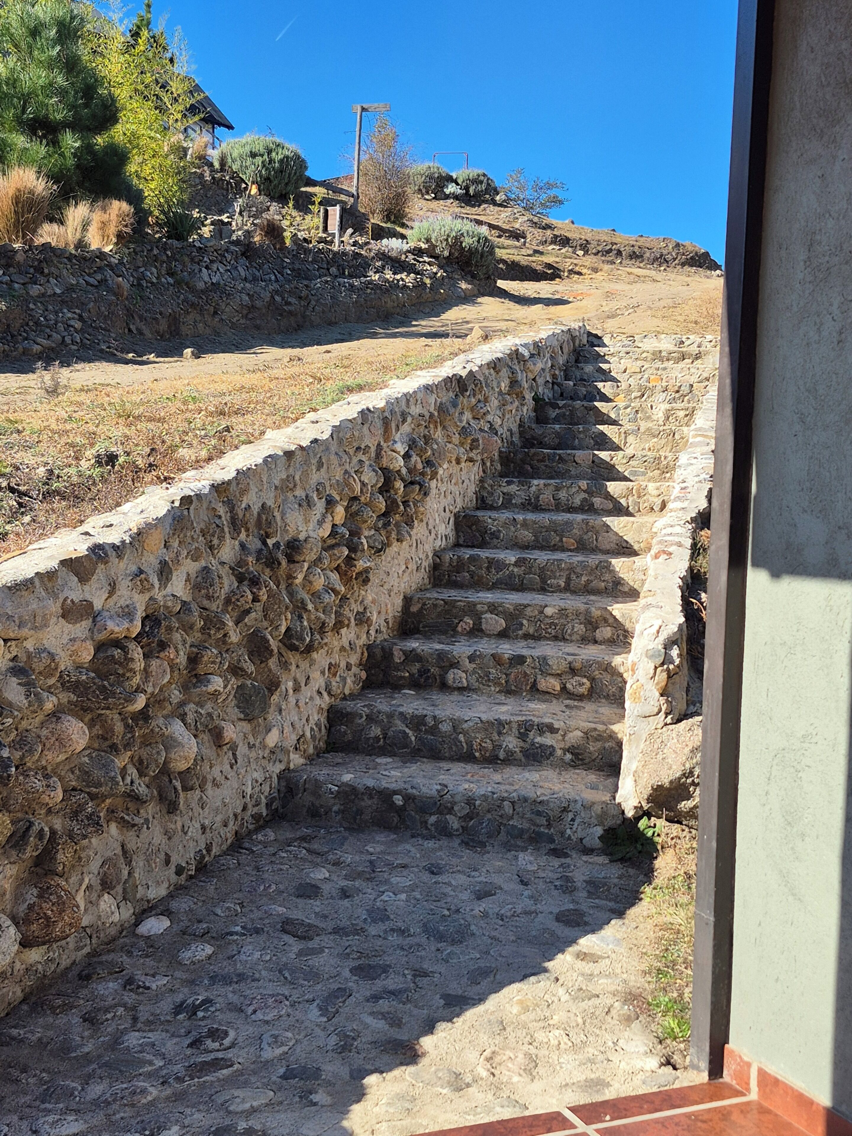 Un escalier en pierre menant vers le haut d’une colline, avec une vue sur une maison et des arbres en arrière-plan.