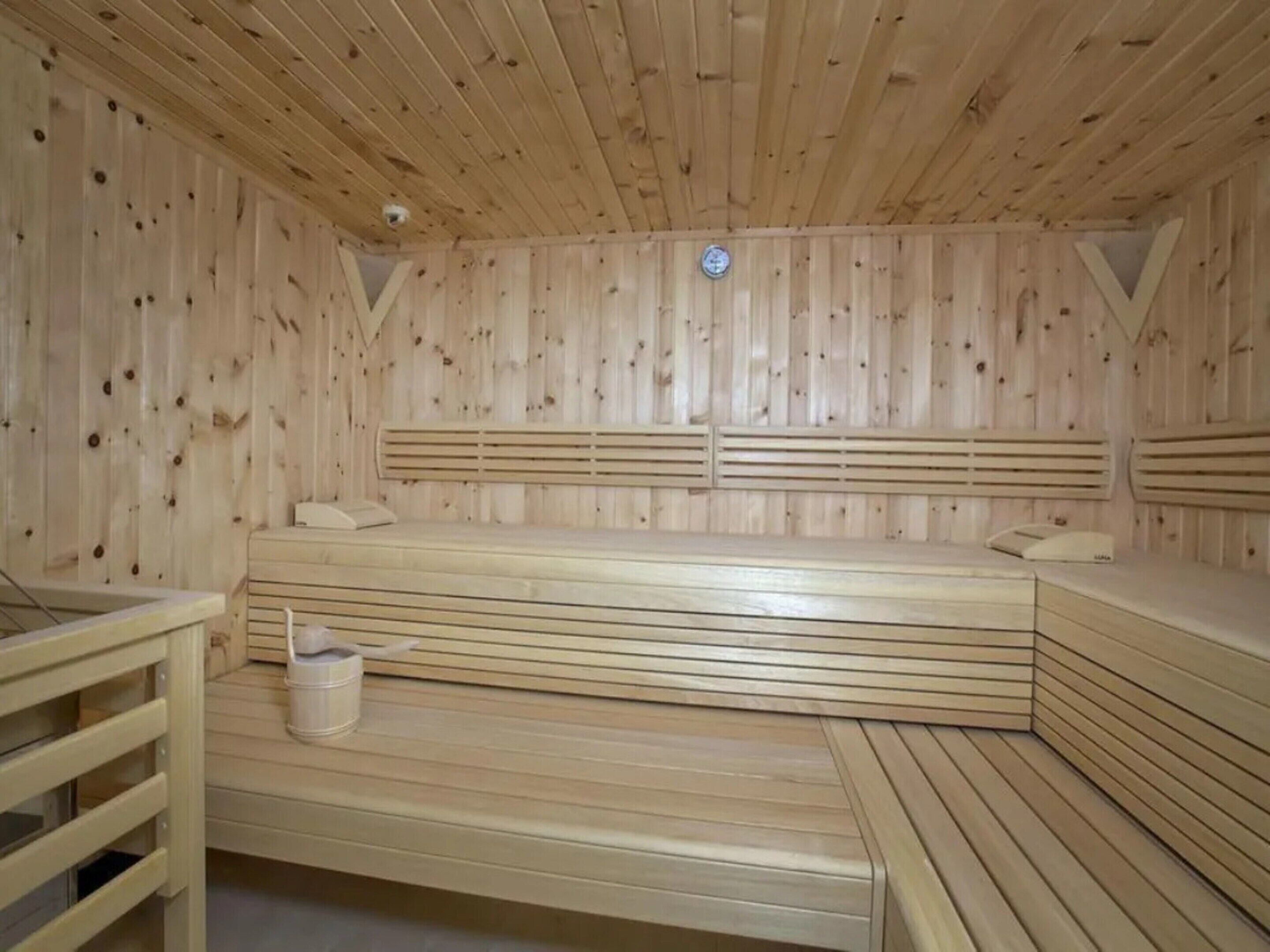 A wooden sauna with benches and a bench seat, a bucket, and a ventilation vent.