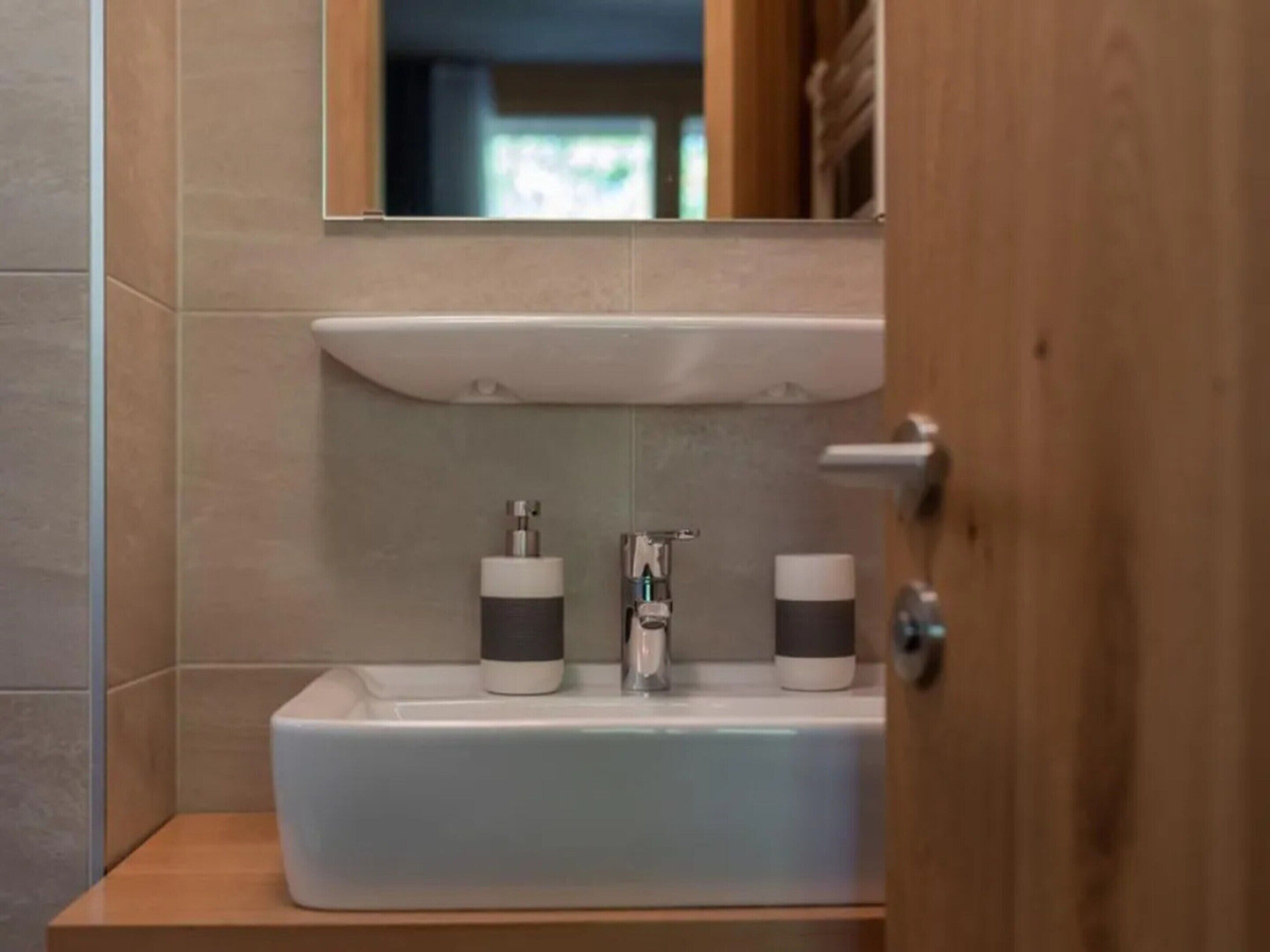 Ein Badezimmer mit einem weißen Waschbecken, zwei Seifenspendern und einem Spiegel darüber.