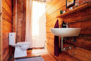 Un baño de madera con inodoro blanco, lavamanos y cortina de ducha.