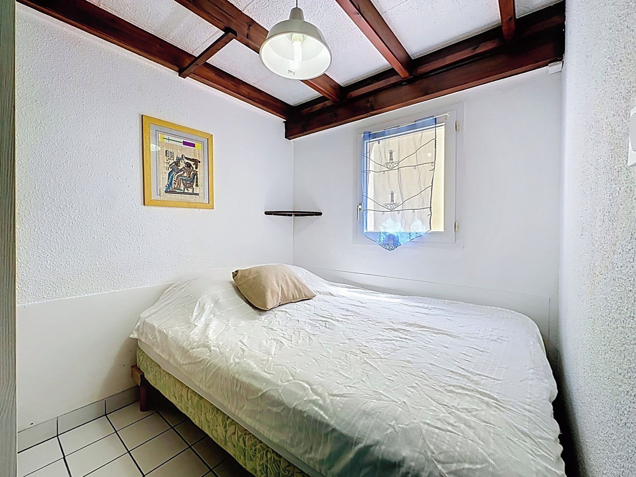 Een slaapkamer met een bed, een ingelijste foto, een raam met gordijn en een plafondventilator.