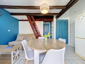 Ein Essbereich mit einem runden Holztisch, weißen Stühlen, einer Vase mit Blumen, einer blauen Wand, einer Holzleiter und einer weißen Tür.