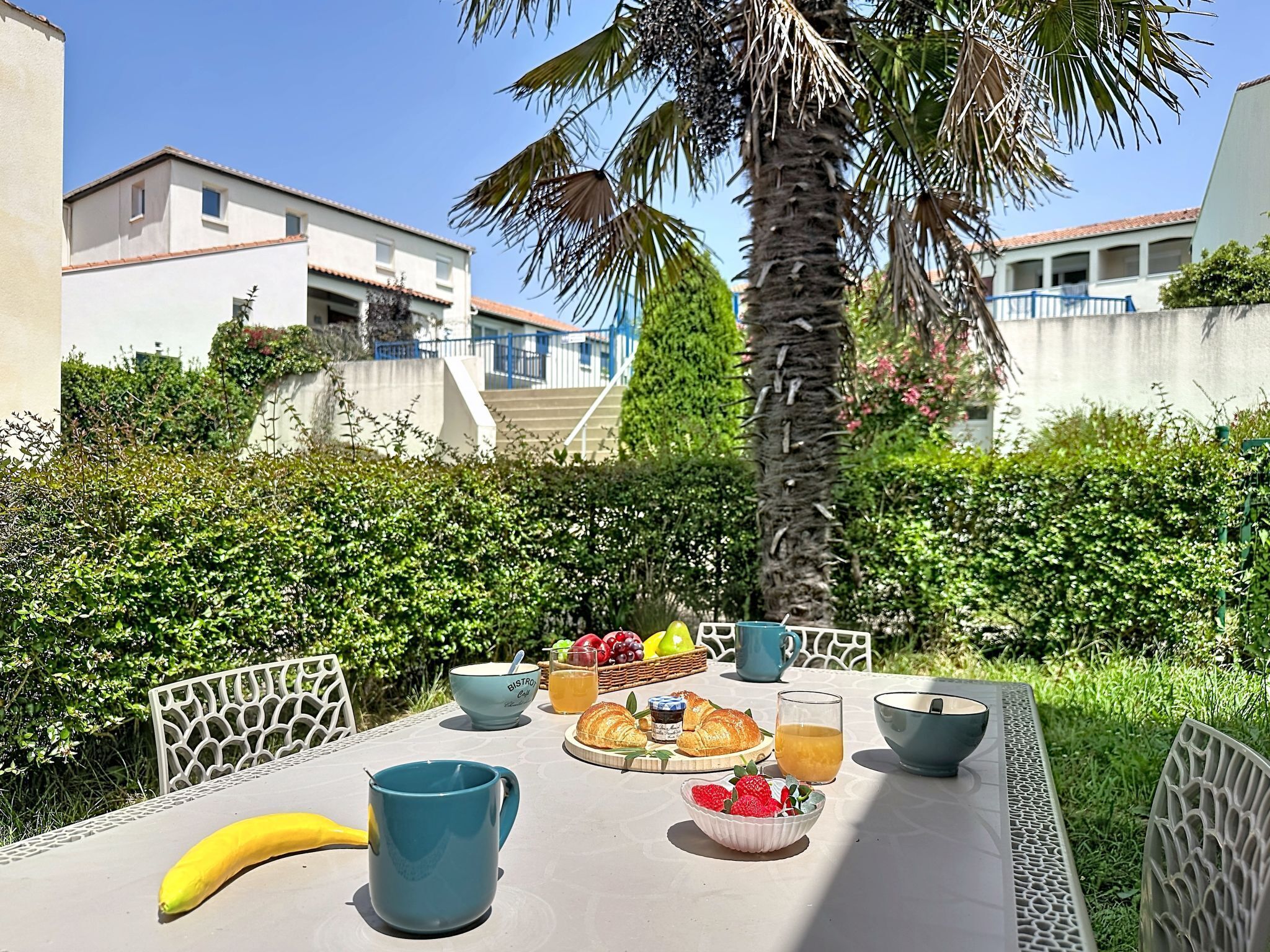 A table set with breakfast items, including a banana, a blue mug, a bowl of strawberries, and a croissant.