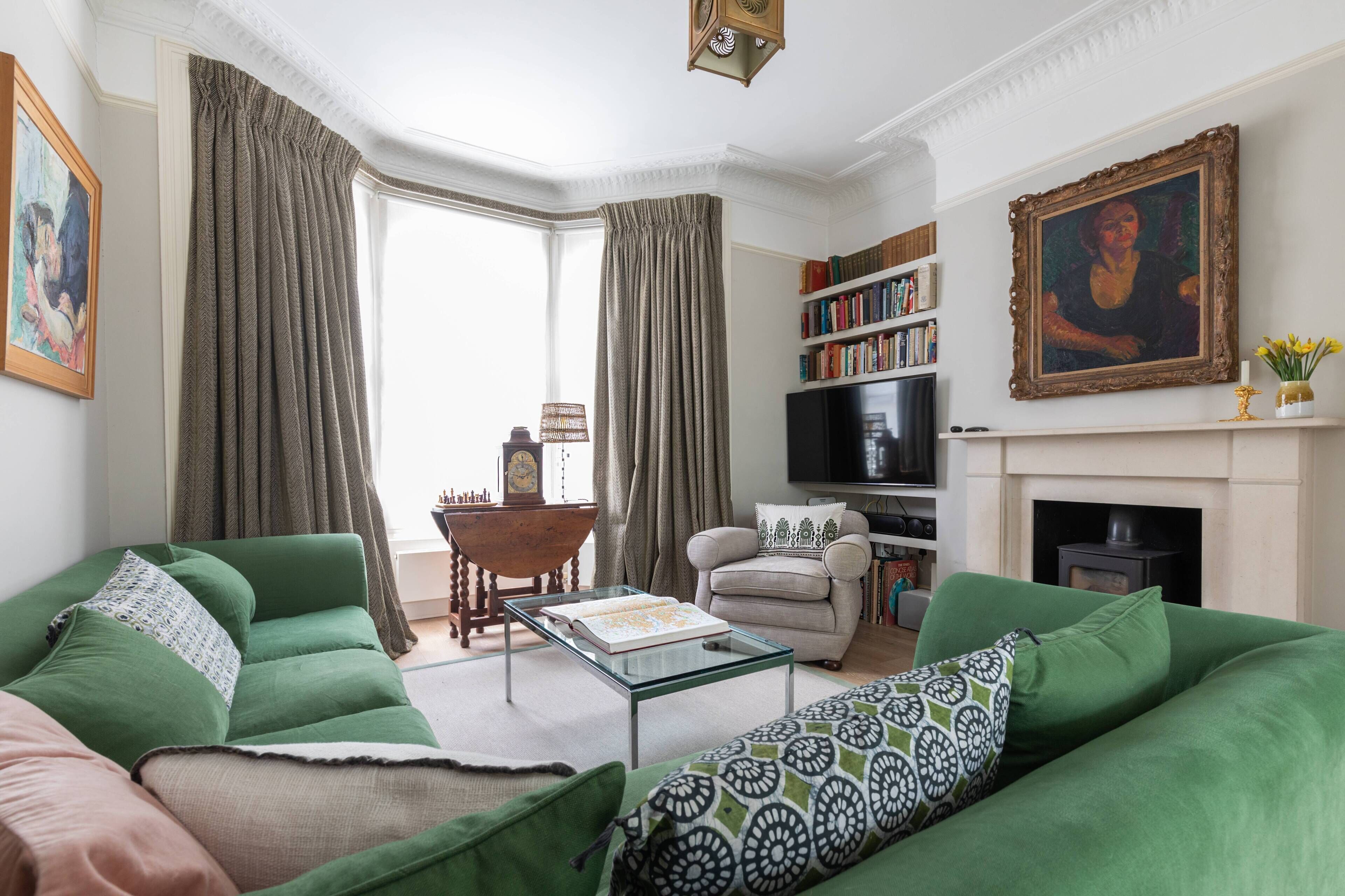 A living room with green sofas, a glass coffee table, a fireplace, a bookshelf, and a painting on the wall.