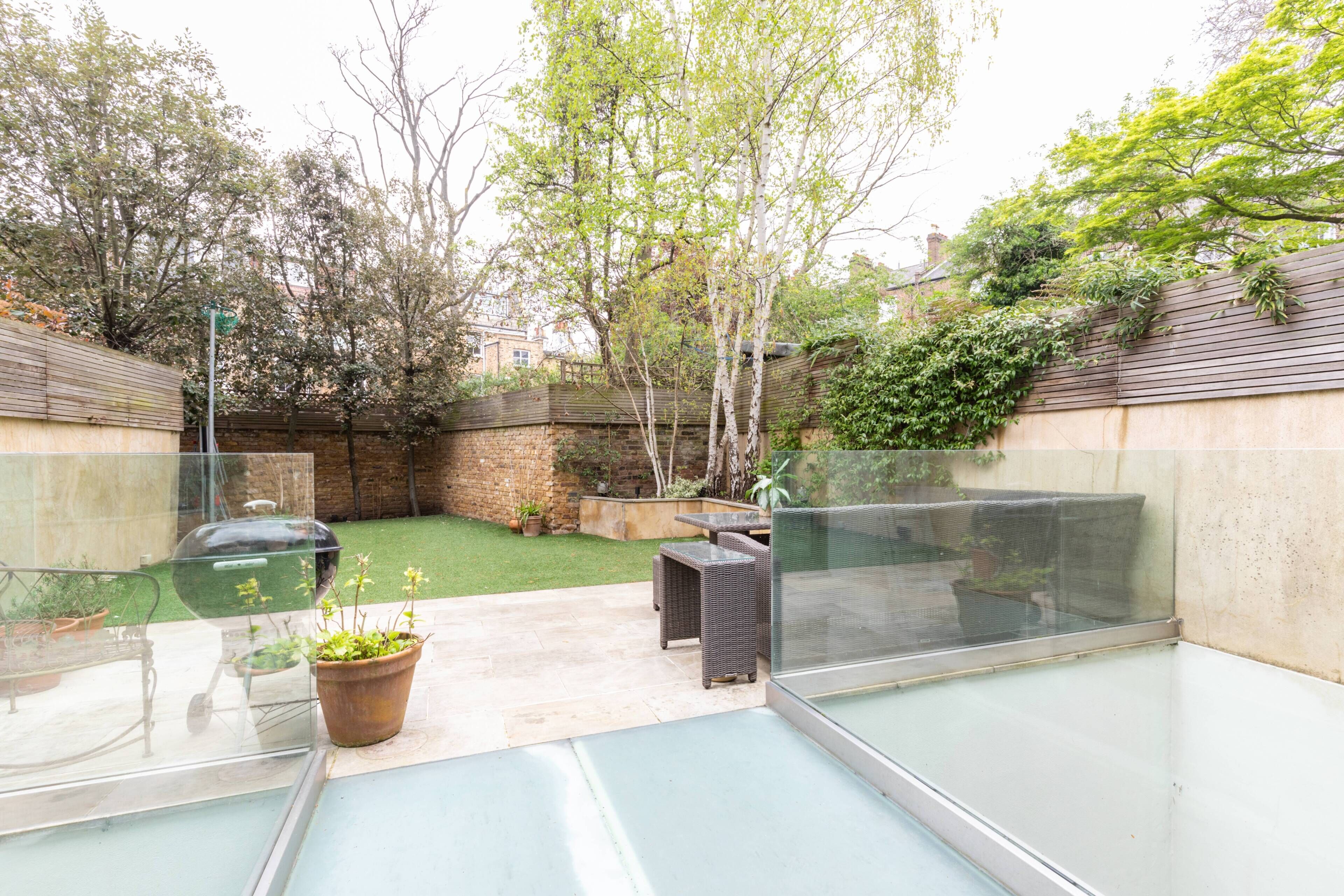 A glass-enclosed balcony with a view of a garden, a seating area with a table and chairs, and a potted plant.