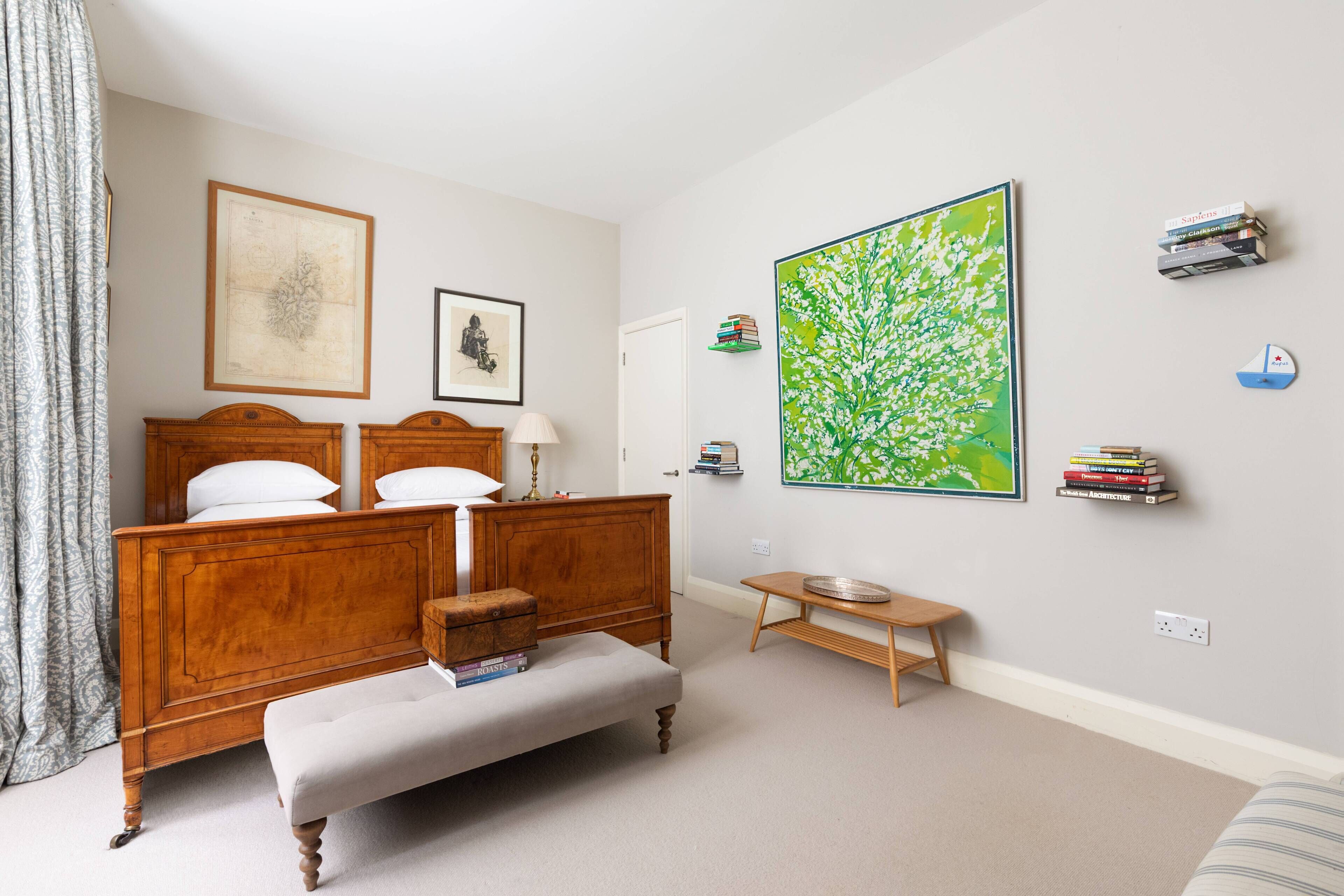Un dormitorio con una cama de madera, un banco, una mesita, un cuadro grande de color verde y una estantería.