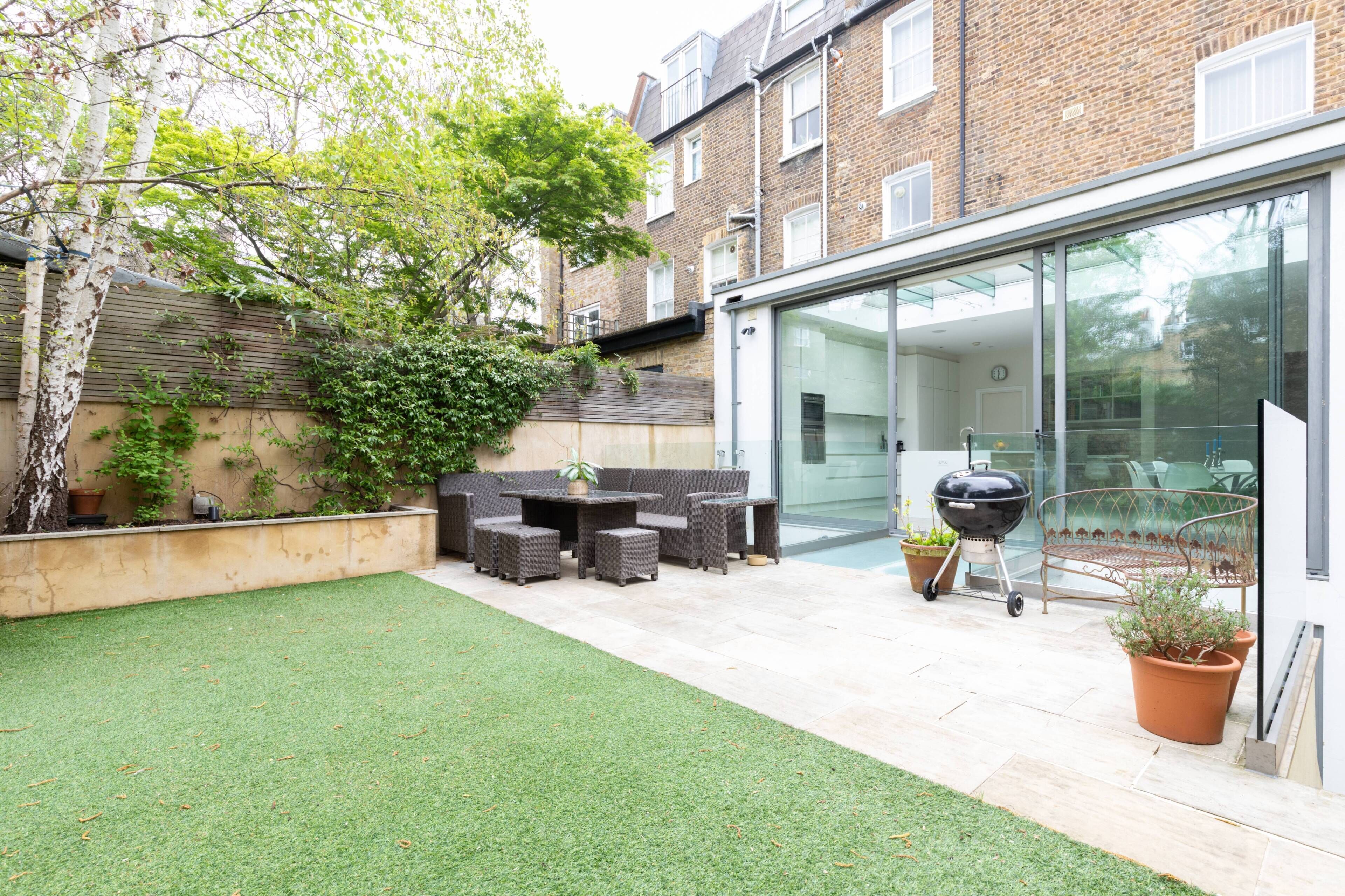 A patio with artificial grass, a dining set, and a barbecue grill.