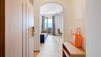 Een gang die uitkomt op een balkon met een bank, gordijnen, een houten bankje en een oranje tas aan de muur.
