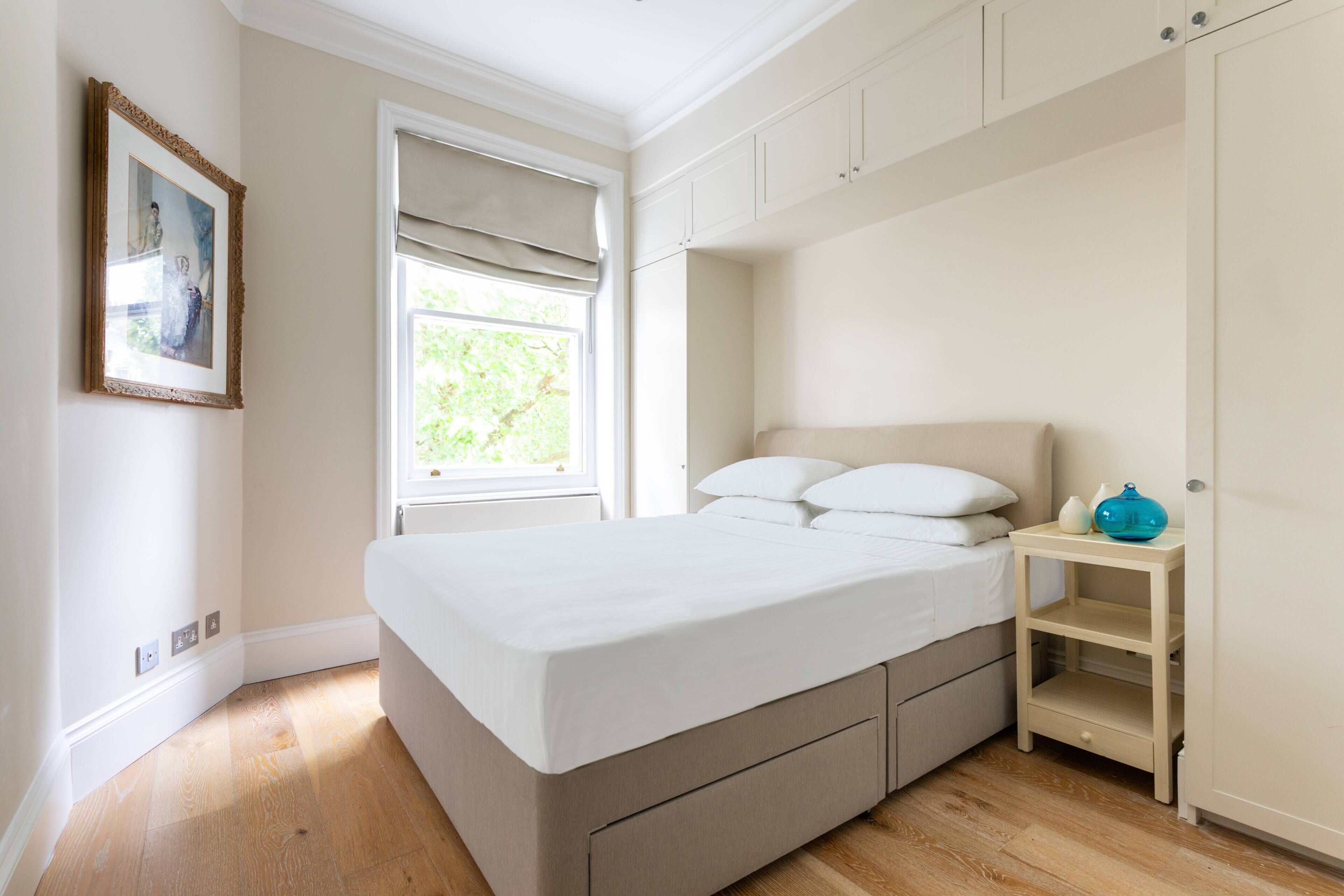 A bedroom with a bed, a nightstand, a wardrobe, and a window with blinds.