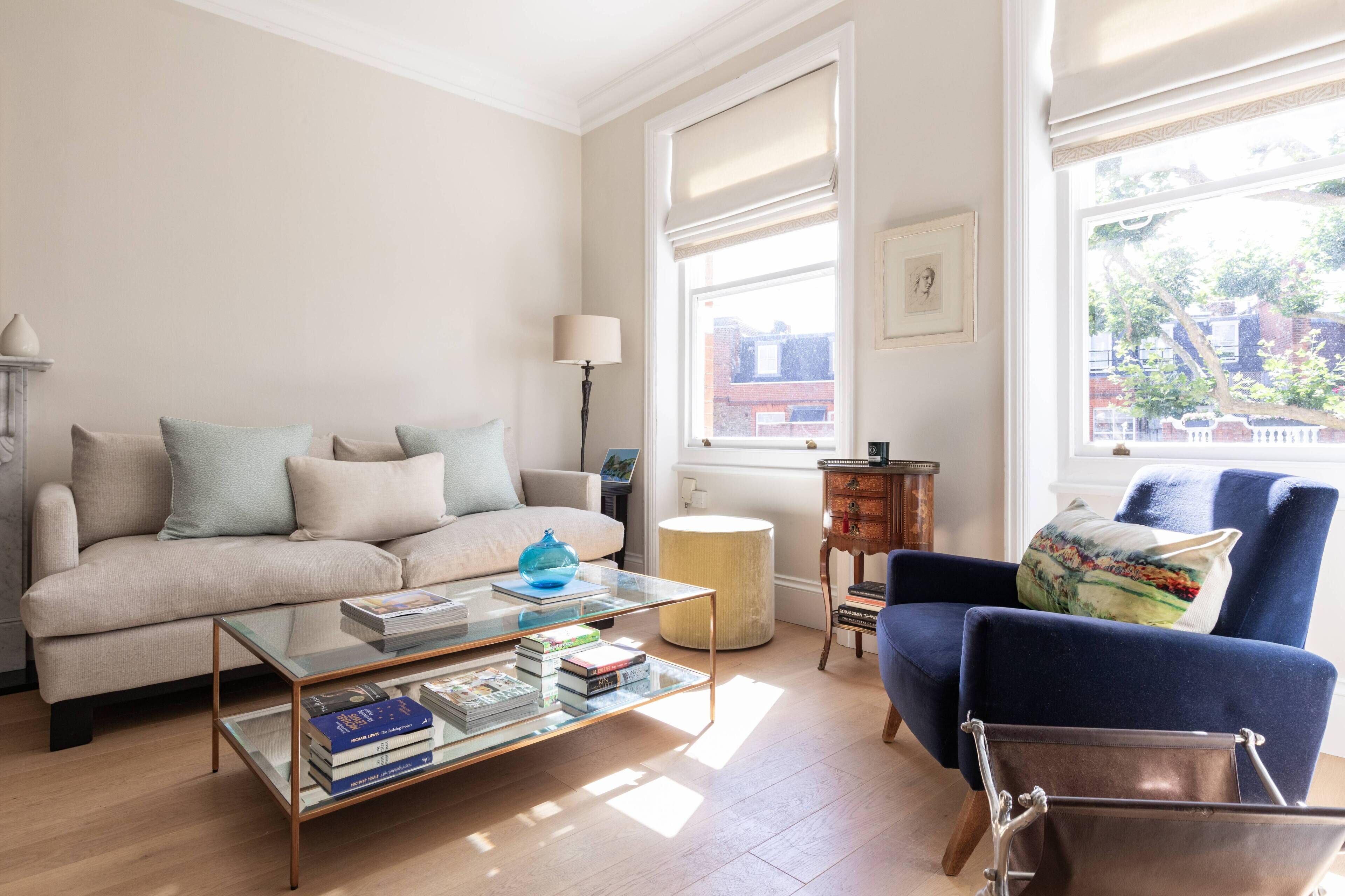 A living room with a sofa, armchair, coffee table, lamp, and a view of buildings outside.