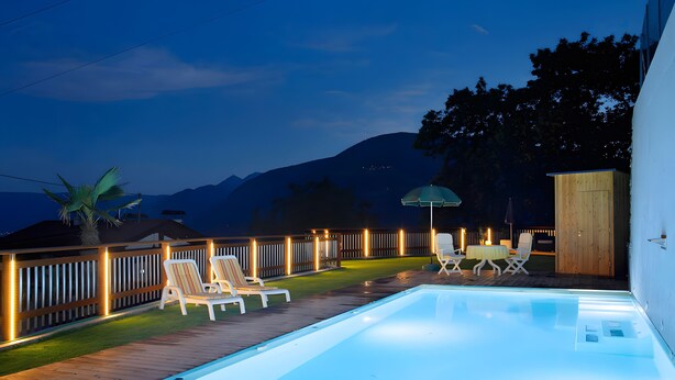 Una piscina con sillas de descanso y una mesa, rodeada por una terraza de madera y un cerco de madera.