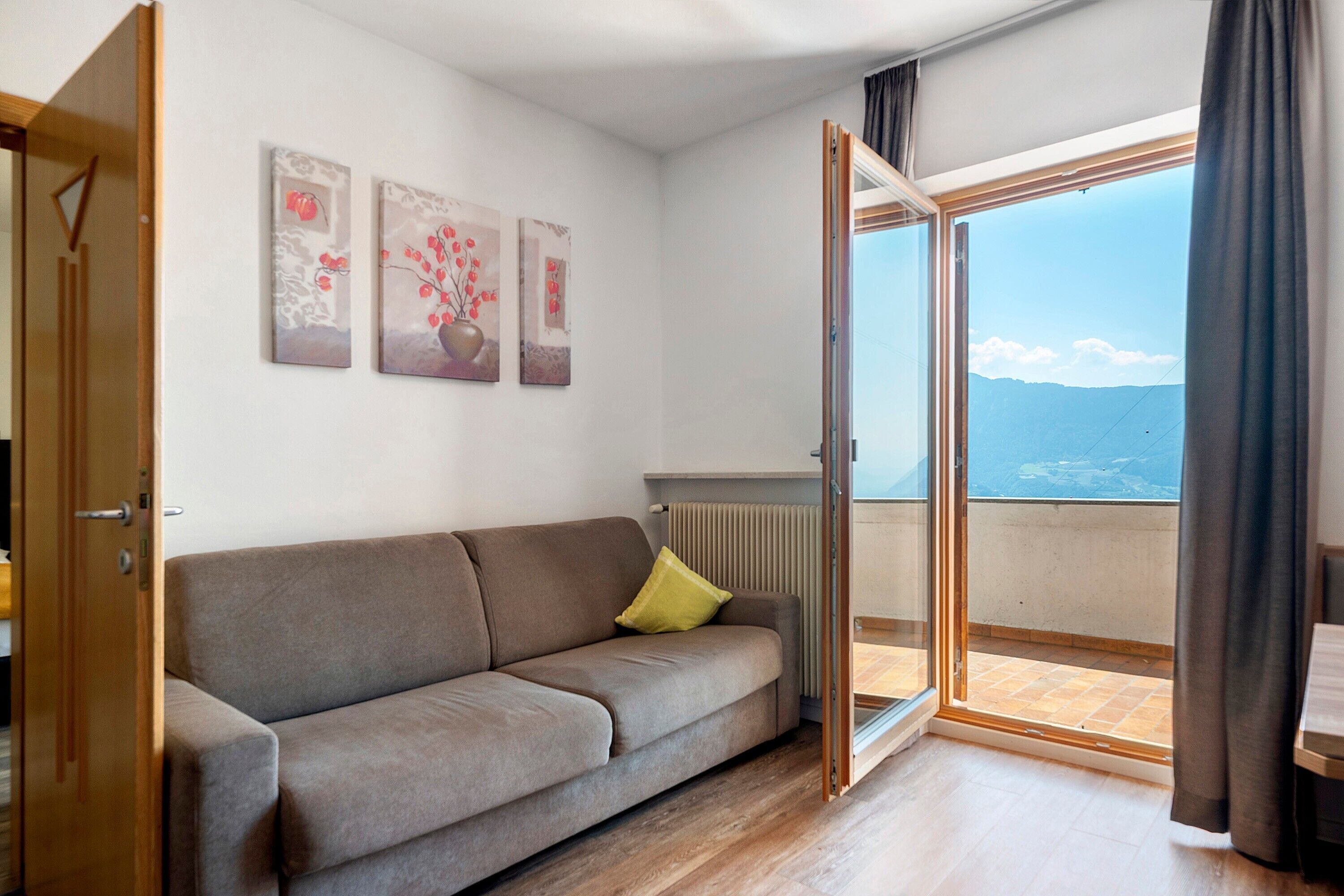 Quarto com sofá, radiador e vista para o mar através de uma porta de vidro.