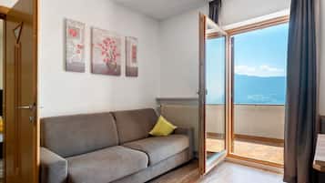 Quarto com sofá, radiador e vista para o mar através de uma porta de vidro.