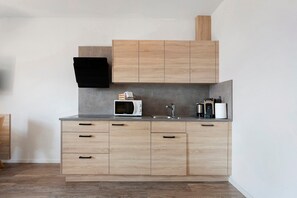 Una cocina moderna con armarios de madera, microondas, lavamanos y cafetera.