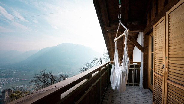 Un balcon en bois offrant une vue sur les montagnes, un hamac suspendu et une porte en bois.