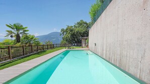 Une piscine rectangulaire avec une terrasse en bois d’un côté, entourée d’une clôture, et une montagne en arrière-plan.