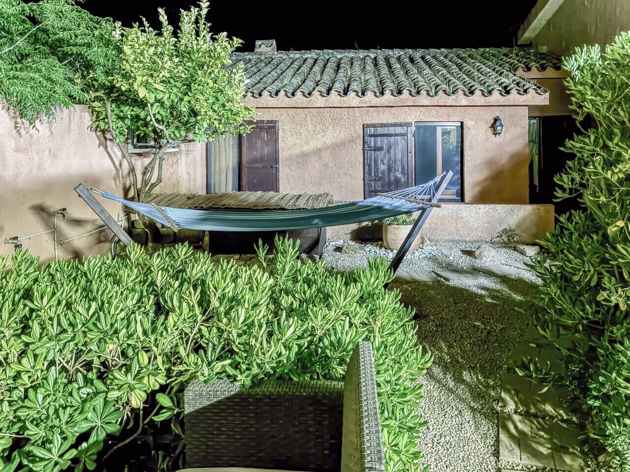 A hammock between two buildings, a tiled roof, and surrounding greenery.
