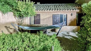 Un hamac tendu entre deux bâtiments, un toit recouvert de tuiles et une végétation luxuriante tout autour.