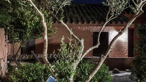 Un bâtiment avec un toit recouvert de tuiles, un panneau solaire et un arbre devant.