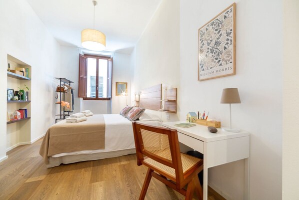 Ein Schlafzimmer mit einem Bett, einem Schreibtisch, einem Stuhl, einem Fenster, einem Regal und einem gerahmten Bild an der Wand.