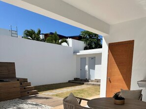 Eine moderne Außenpatio mit einem Holztisch und -stühlen, einer kleinen Gartenanlage und einem weißen Gebäude mit einer Holztür.