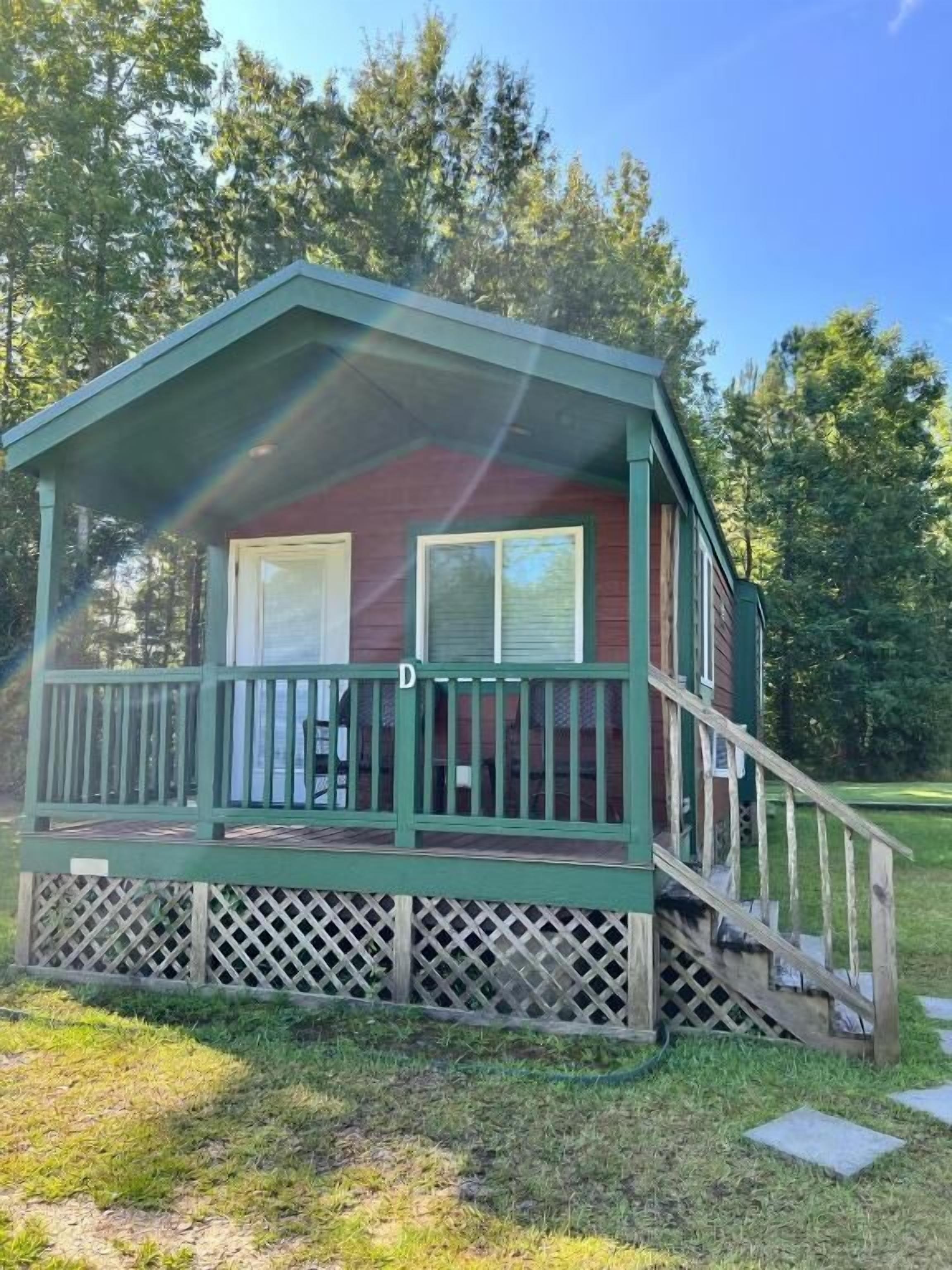 A small, single-story cabin with a porch, a staircase leading to the entrance, and a fenced yard.