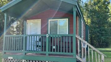 A small, single-story cabin with a porch, a staircase leading to the entrance, and a fenced yard.