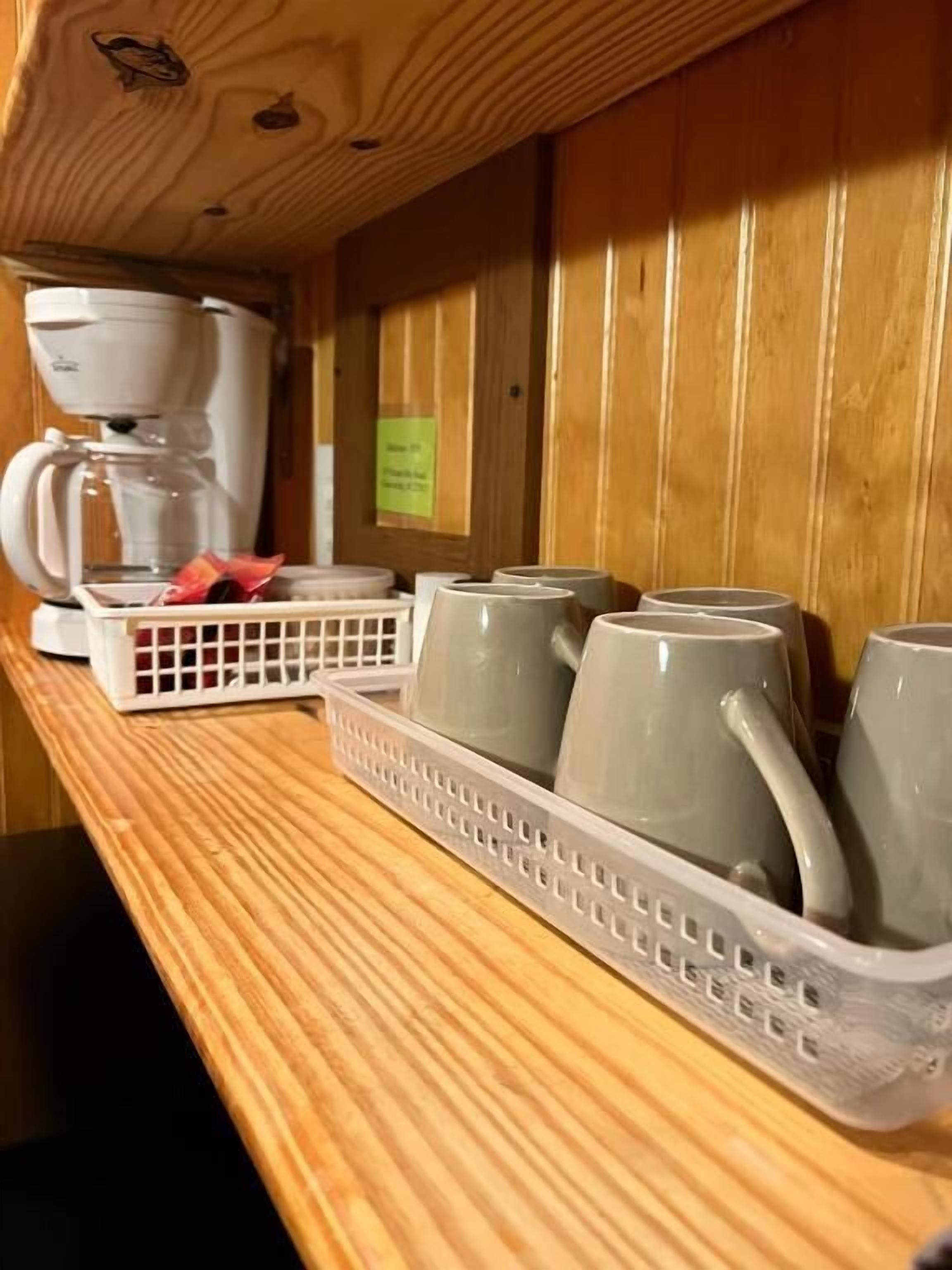 Une étagère en bois avec une machine à café, un plateau rempli de tasses et un petit panneau.