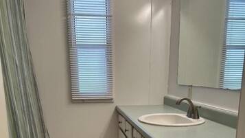 Ein Badezimmer mit Waschbecken, Spiegel, Schränken und einem Fenster mit Jalousien.