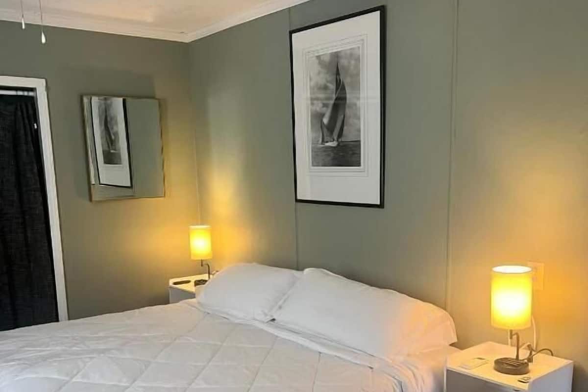 Un dormitorio con una cama, mesitas de noche, un ventilador de techo y obras de arte colgadas en la pared.