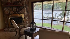 Una chimenea de piedra, una mesa con un farol, y vistas de un lago a través de amplios ventanales.