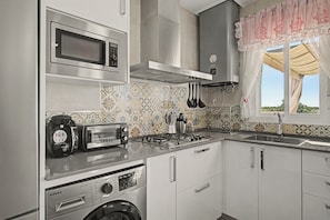 A compact kitchen with a microwave, toaster, gas stove, and washing machine. - 'El Desafío' Apartment with Private Terrace and Wi-Fi (Roche)