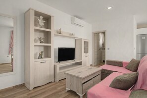 A modern living room with a flat-screen TV, wooden furniture, and a pink sofa. - 'El Desafío' Apartment with Private Terrace and Wi-Fi (Roche)