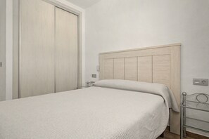 Un lit simple avec une tête de lit en bois, dans une pièce aux murs blancs et dont la porte est fermée.