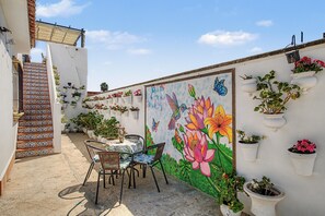 Une terrasse avec une table et des chaises, une fresque ornée de fleurs et de papillons, et un escalier avec des carreaux décoratifs.